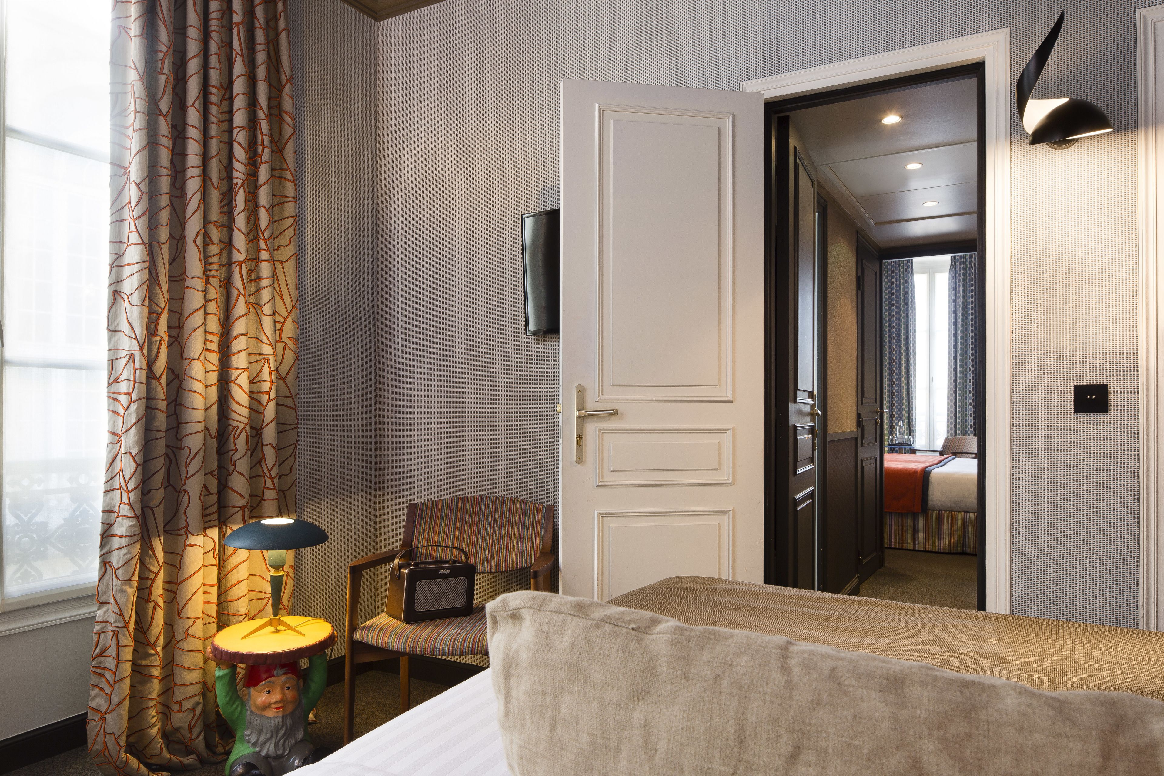 A hotel room with a bed, a chair, a lamp, and a door leading to another room.