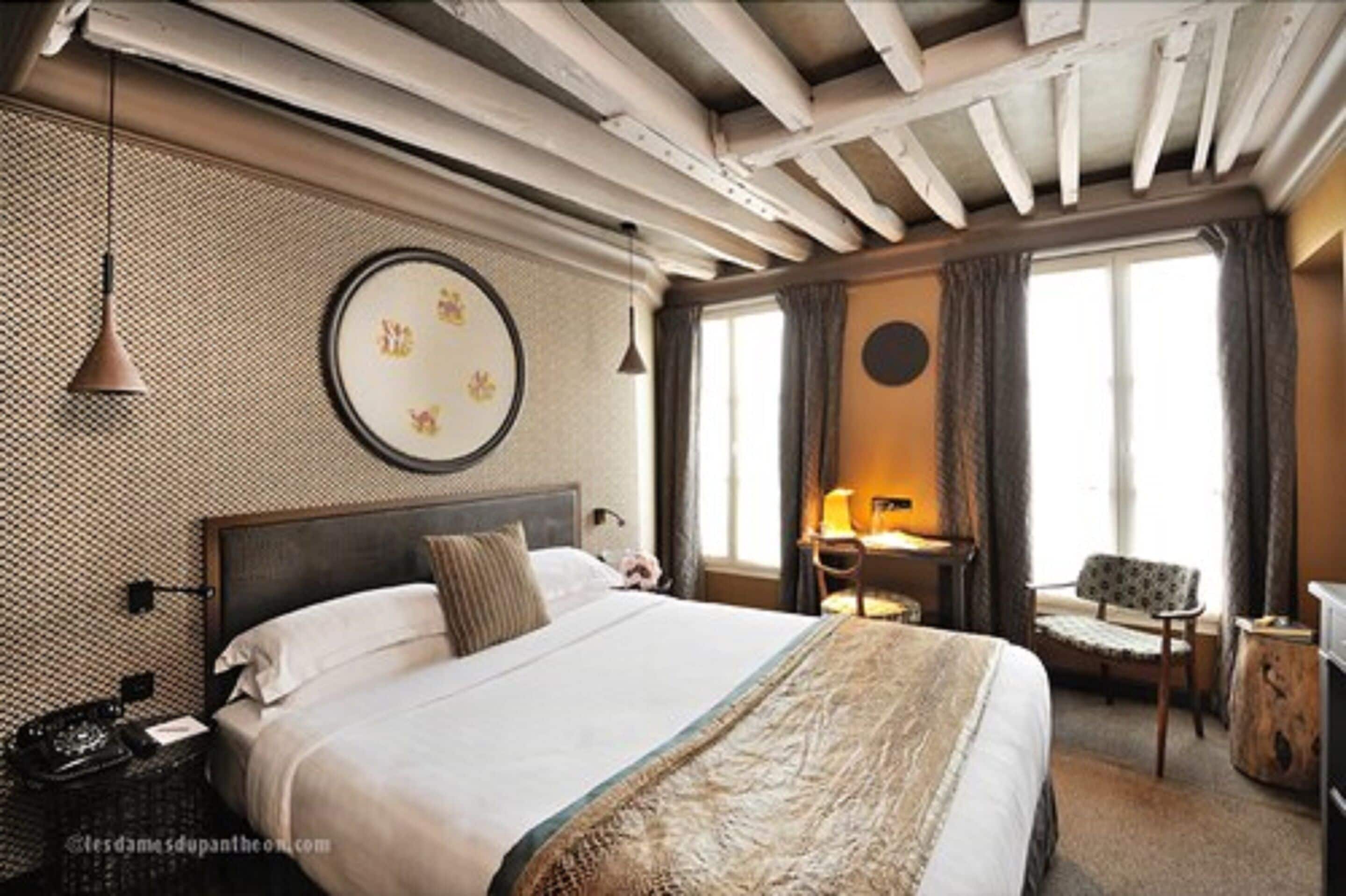 A hotel room with a large bed, a desk with a lamp, a chair, and a window with curtains.