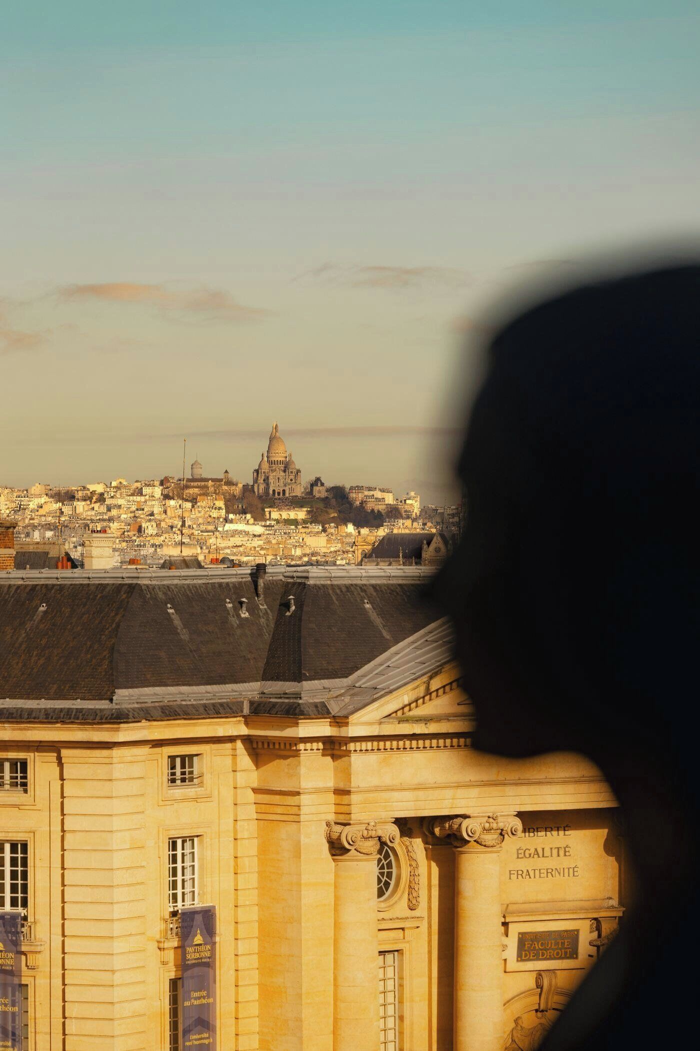 A view of a cityscape with a prominent building in the background and a silhouette of a person in the foreground.