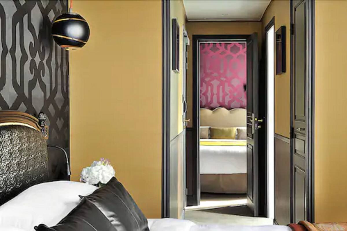 A hotel room with a bed, a nightstand, and a door leading to another room.