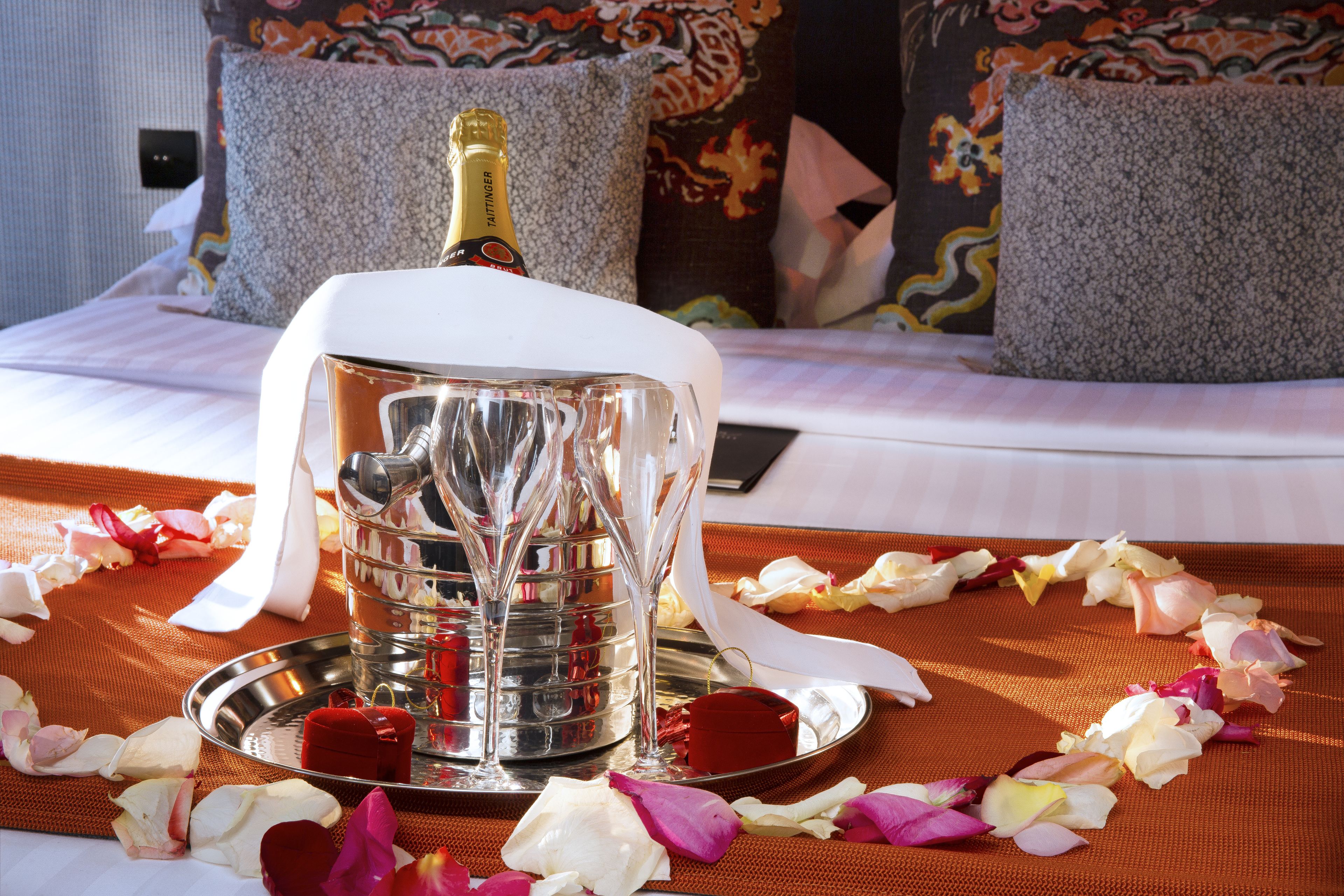 A bed with a decorative tray, a bottle of champagne, and rose petals.
