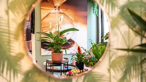 A circular mirror reflecting a room with a large hourglass, potted plants, and a small table. - Hotel Ariane Montparnasse by Patrick Hayat (Paris)