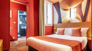 A hotel room with a large bed, a wooden headboard, and a red carpet. - Hotel Ariane Montparnasse by Patrick Hayat (Paris)