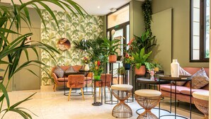A modern lounge area with a sofa, round tables, and potted plants. - Hotel Ariane Montparnasse by Patrick Hayat (Paris)