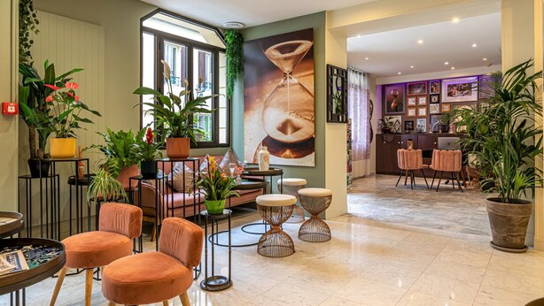 A spacious lobby with a large window, multiple seating areas, and a variety of plants. - Hotel Ariane Montparnasse by Patrick Hayat (Paris)