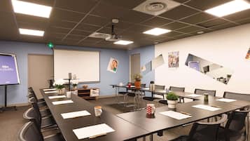 Una sala de conferencias con una larga mesa, sillas, una pantalla de proyector y una pizarra.