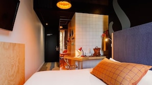 A hotel room with a bed, a desk with a chair, a hanging light fixture, and a tiled wall. - Greet Hotel  Lyon Confluence (Lyon)