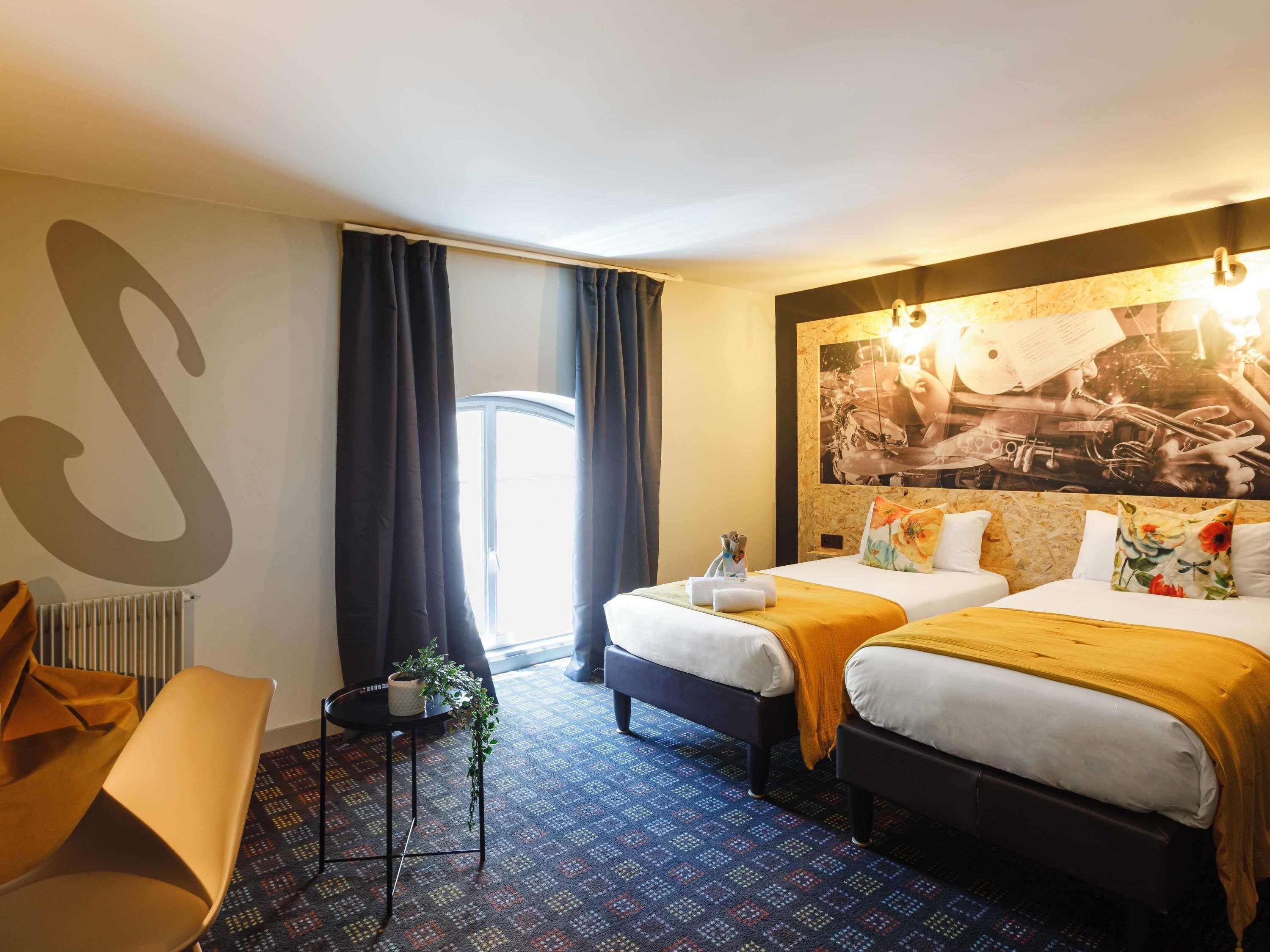 A hotel room with two beds, a large wall mural, a radiator, and a window with curtains.