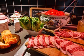 Une table de buffet proposant divers aliments, notamment des viandes tranchées, un saladier de tomates et un saladier de laitue.