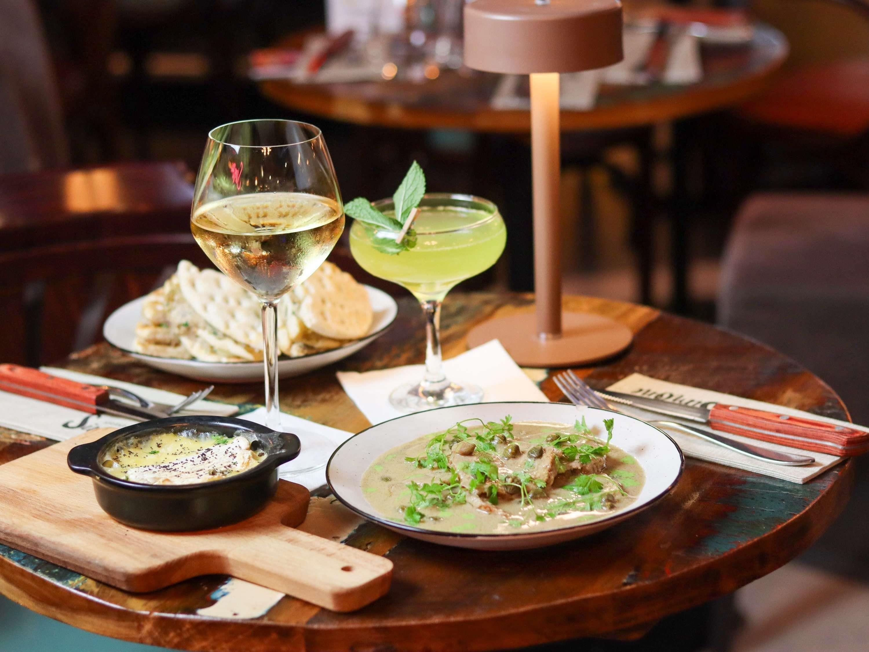 A dining table with a plate of soup, a bowl of soup, a glass of white wine, and a cocktail.