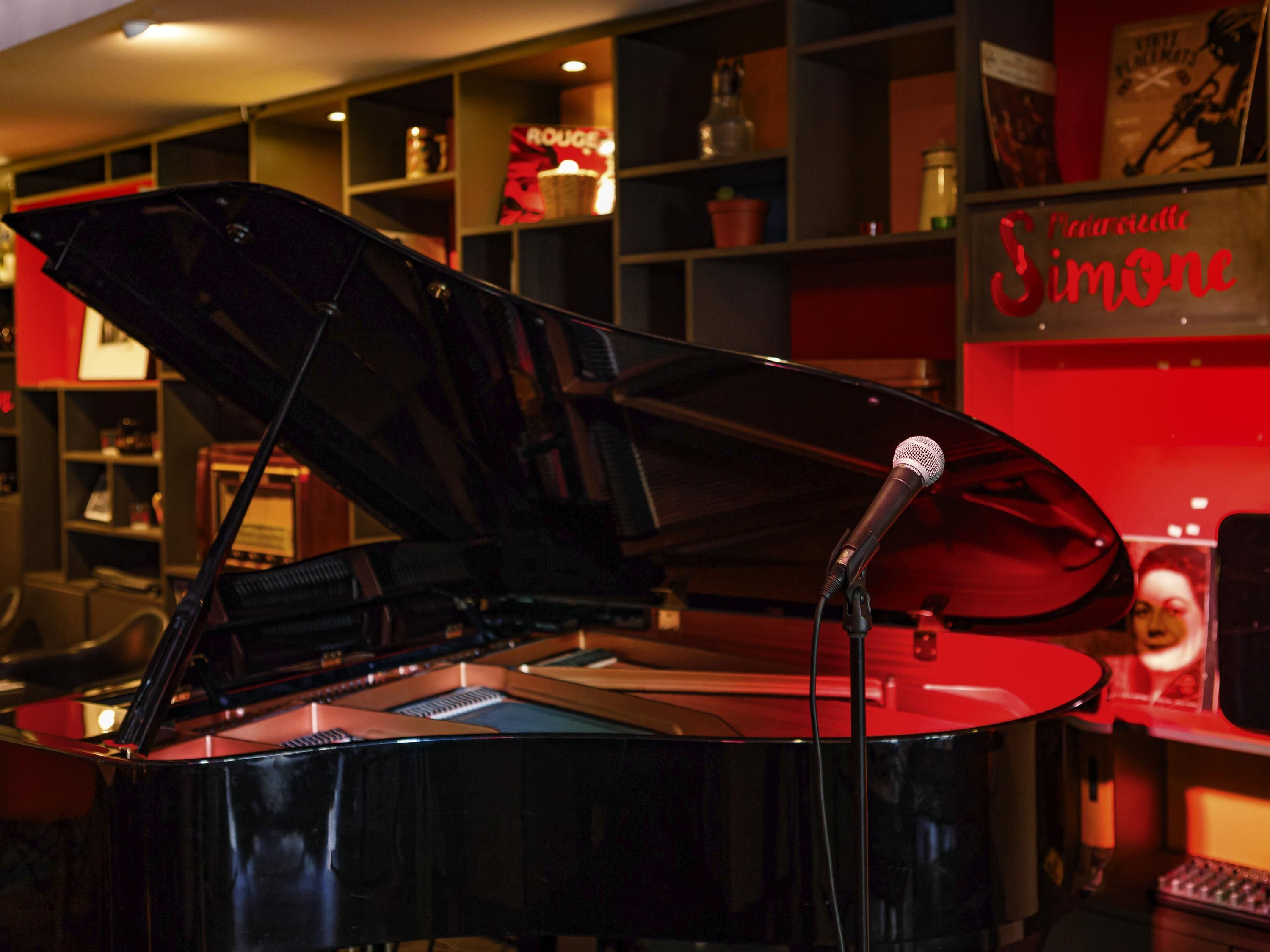 Un piano de cola en una habitación con estanterías y un letrero que dice 'Simone'.