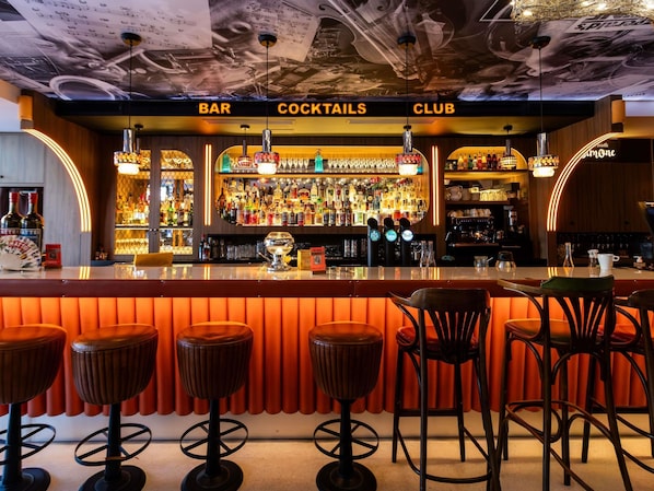 A bar area with stools, a bar counter, and shelves stocked with bottles.