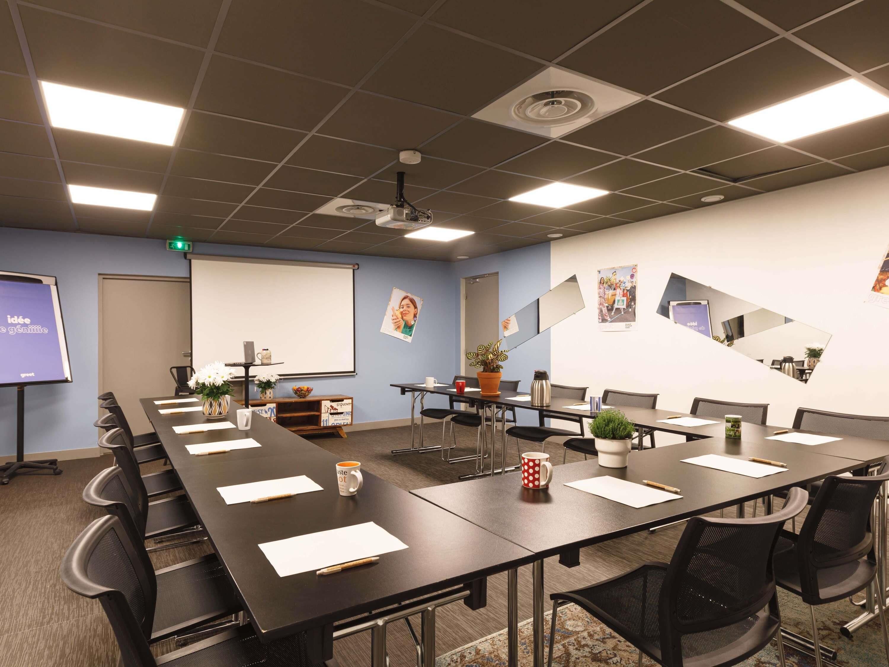 A conference room with a long table, chairs, a projector screen, and a whiteboard.