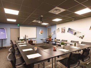 A conference room with a long table, chairs, a projector screen, and a whiteboard. - Greet Hotel  Lyon Confluence (Lyon)