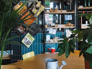 L’intérieur d’un café, avec une table en bois, un arrosoir en métal et divers objets disposés sur des étagères.