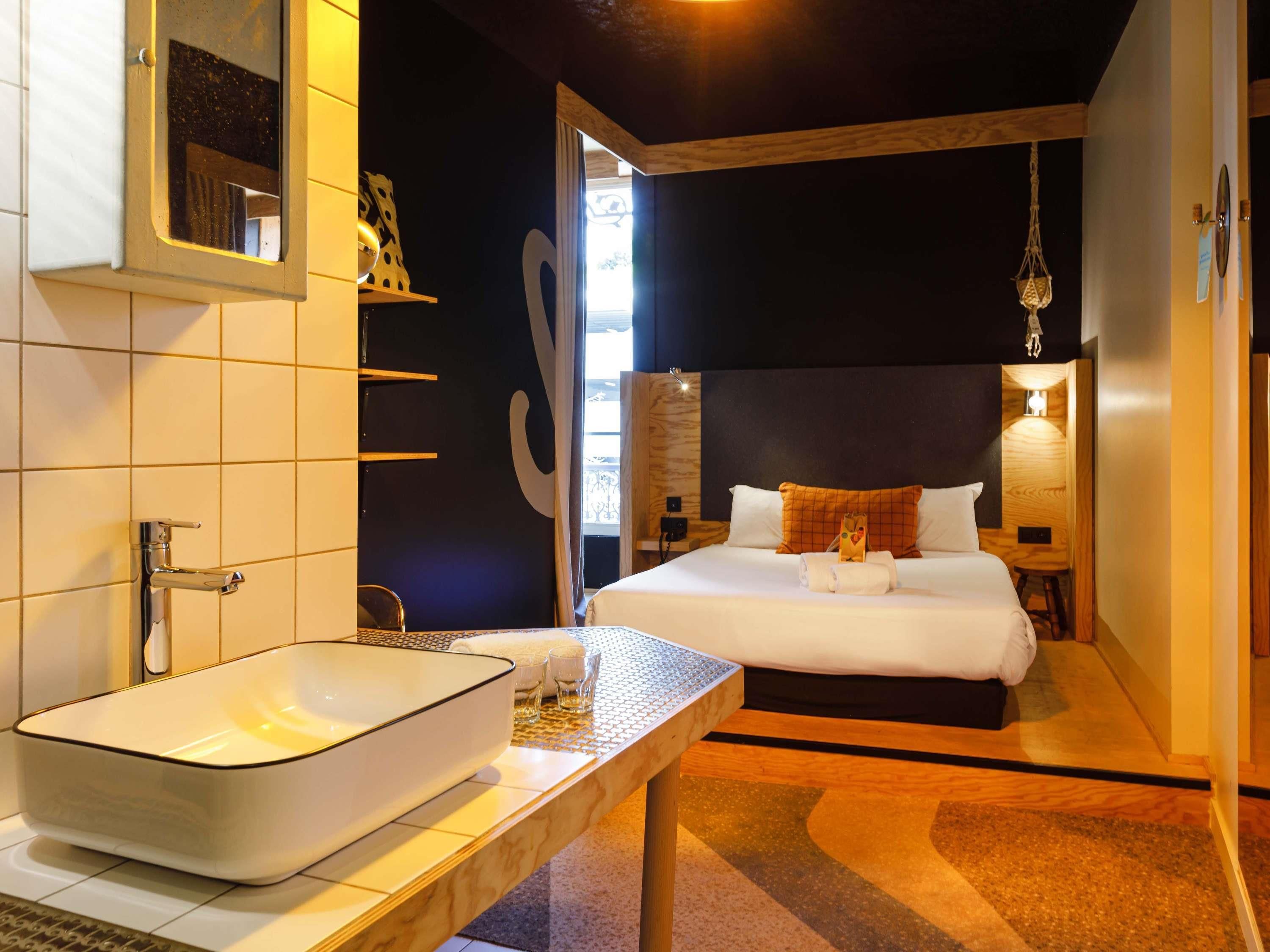 Une chambre d’hôtel moderne avec un grand lit, une table de chevet dotée d’un lavabo blanc et une vue sur l’extérieur.