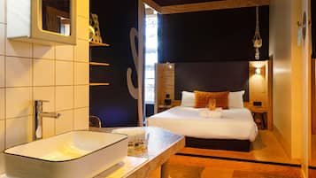 Una habitación de hotel moderna con una cama grande, una mesita de noche con lavamanos blanco y vistas al exterior.