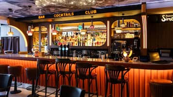 Una zona de bar con taburetes, una barra y una variedad de botellas y vasos.