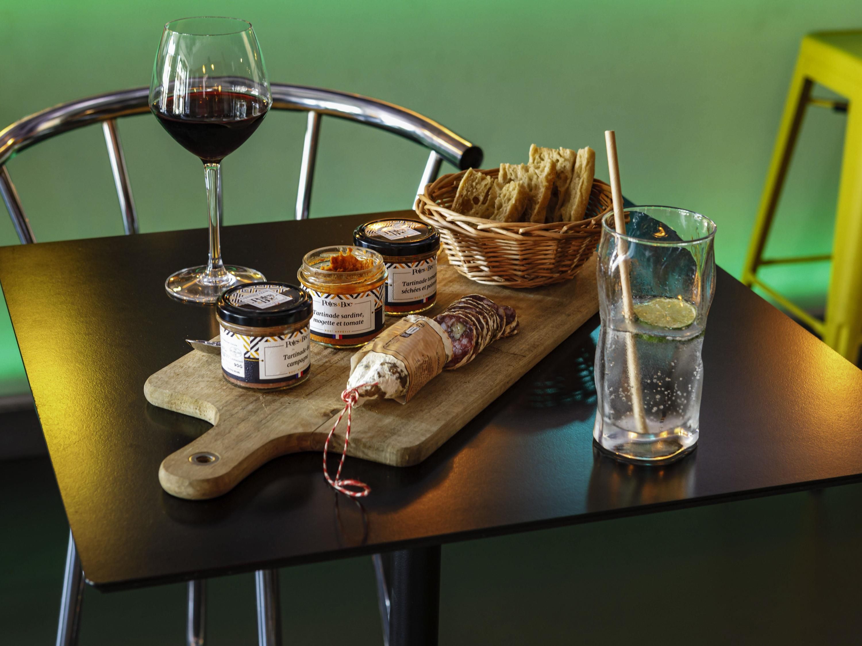 A table with jars of food, a glass of wine, a glass of water, and a basket of bread.