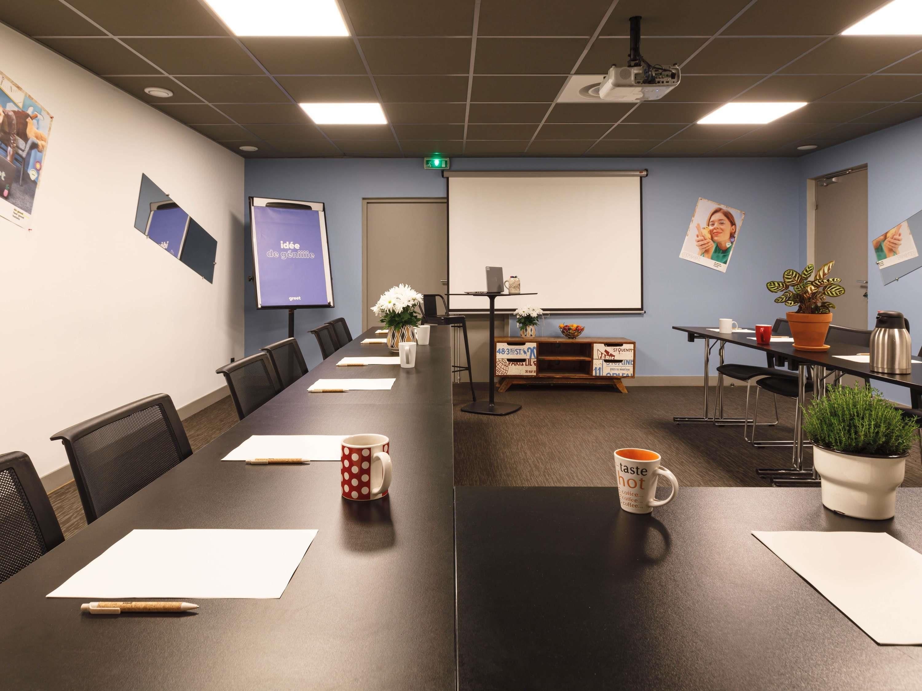 Un salón de conferencias con una mesa larga, sillas, un proyector, una pantalla y varios objetos decorativos.