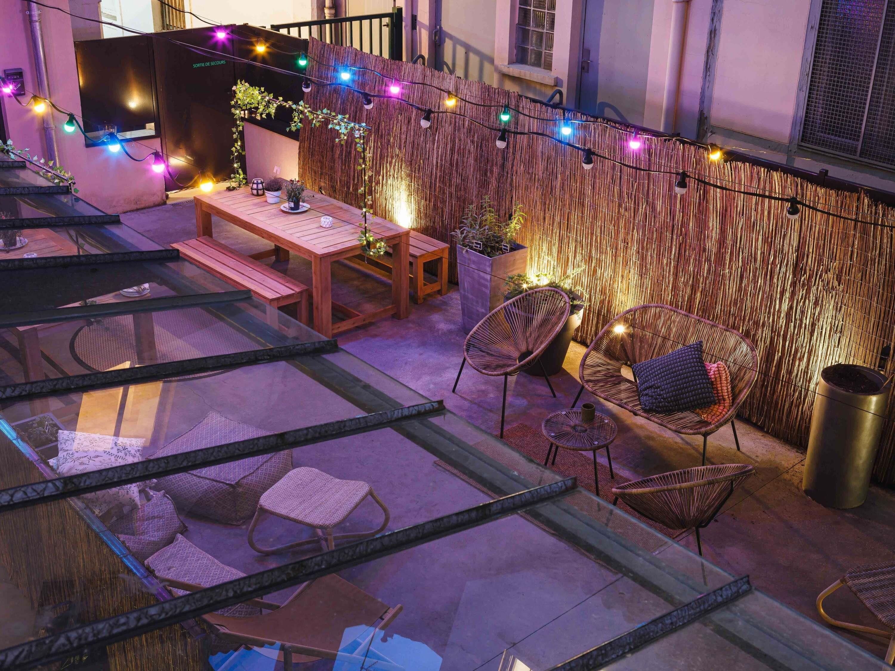 Una terraza en la azotea con una mesa de madera, sillas de mimbre y luces colgantes.
