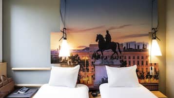 A hotel room with two beds, a nightstand, a lamp, a painting of a horse statue, and a cityscape view.