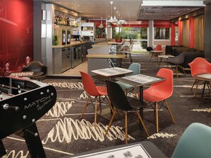 A modern restaurant with a bar area, multiple seating options including tables and chairs, and a visible kitchen in the background. - ibis Lyon Gerland Rue Merieux (Lyon)