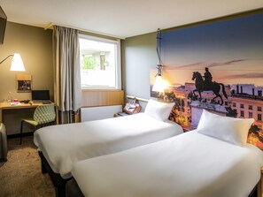 A hotel room with two beds, a desk, a chair, a lamp, and a large cityscape mural on the wall. - ibis Lyon Gerland Rue Merieux (Lyon)