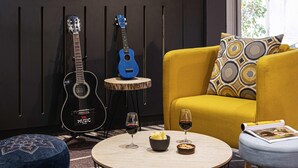 A room with a yellow sofa, a blue guitar, a round table with wine glasses, and a blue ottoman. - ibis Lyon Gerland Rue Merieux (Lyon)