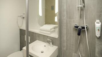 Un baño moderno con cabina de ducha de vidrio, un lavamanos blanco y un inodoro.