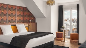 Une chambre moderne avec un lit, une tête de lit en bois, un luminaire suspendu et une vue sur la ville par une grande fenêtre.