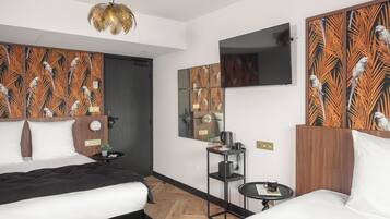 A modern hotel room with two beds, a small table, a mirror, and a television on the wall.