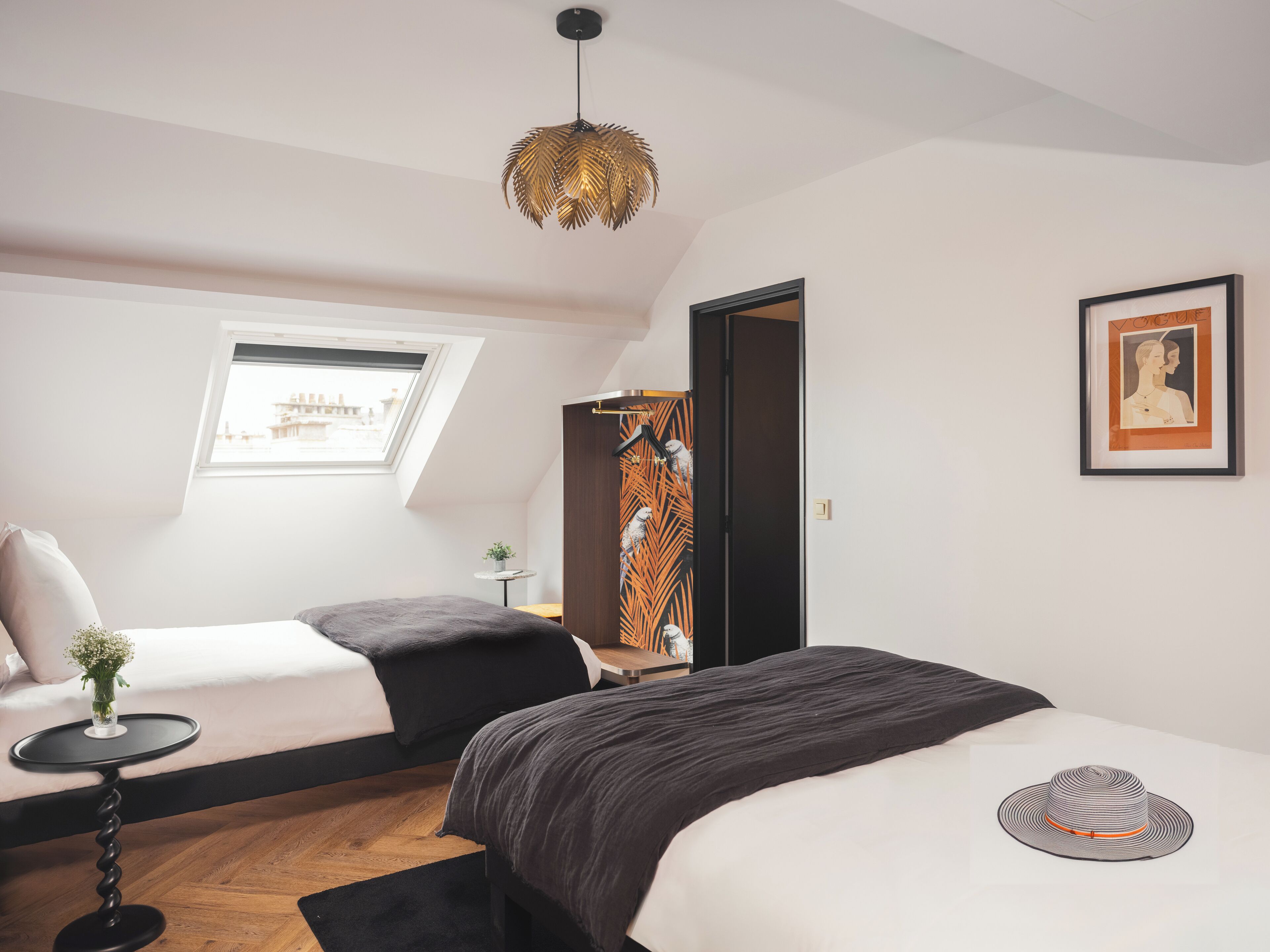 A modern bedroom with two beds, a small table, a hanging light fixture, and a framed picture on the wall.