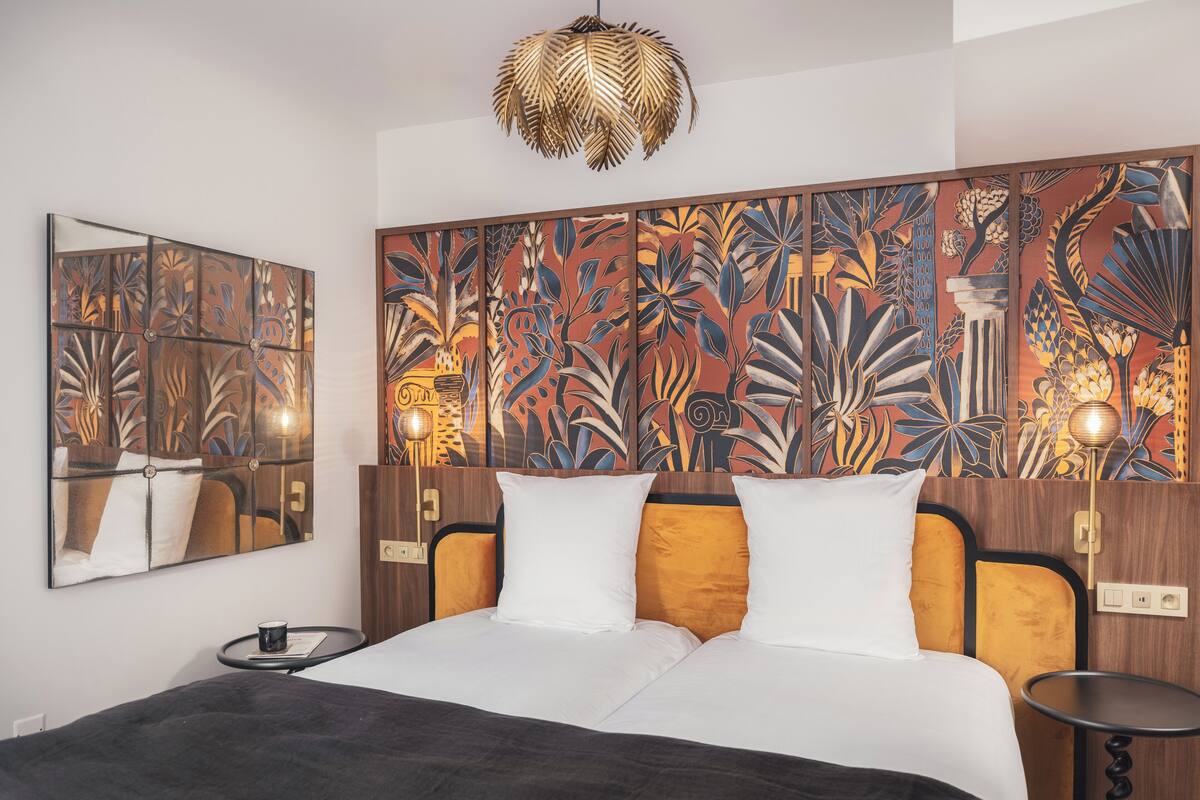 A hotel room with a large bed, a wooden headboard, a wall mural, a round table, and a hanging light fixture.