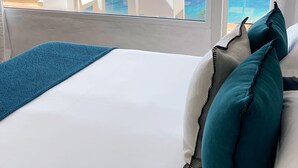 Un dormitorio con cama, almohadas blancas y vistas al mar y a las montañas.
