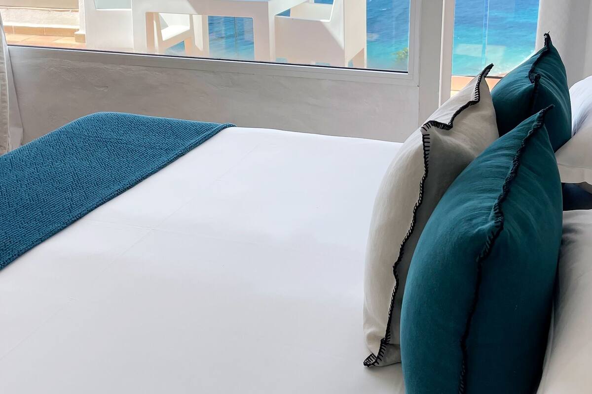 Une chambre à coucher avec un lit, des oreillers blancs et une vue sur la mer et les montagnes.