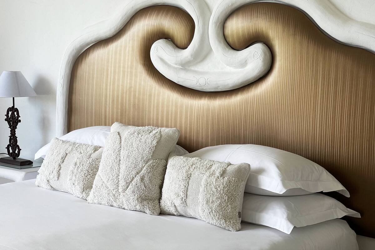 Une chambre à coucher avec une tête de lit classique, du linge de lit blanc et une lampe de chevet.