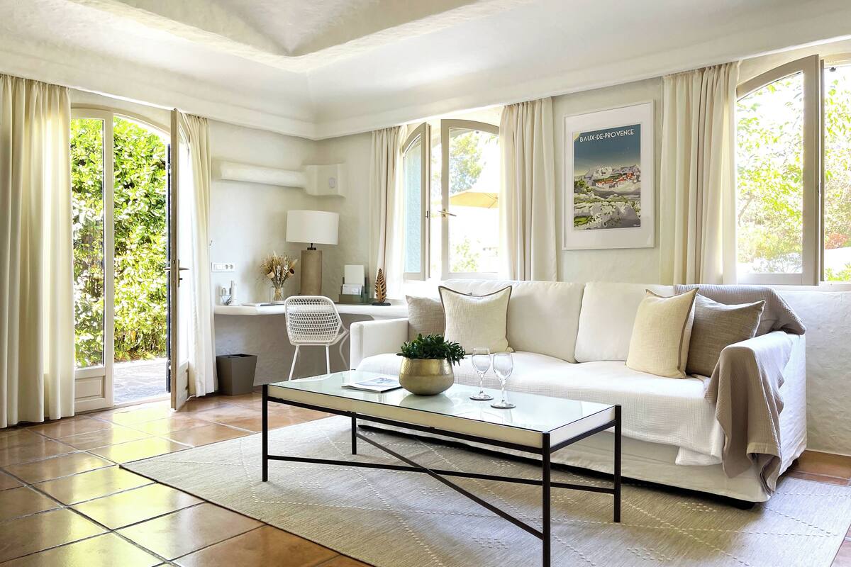 Un salon moderne avec un canapé blanc, une table basse en verre et une vue sur la verdure à l’extérieur.