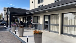 A modern building with a covered outdoor seating area, large windows, and potted plants. - The Originals City, Hôtel Orléans Nord (Saran)
