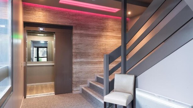 A modern interior with a staircase, a chair, and a door leading to another room. - The Originals City, Hôtel Orléans Nord (Saran)