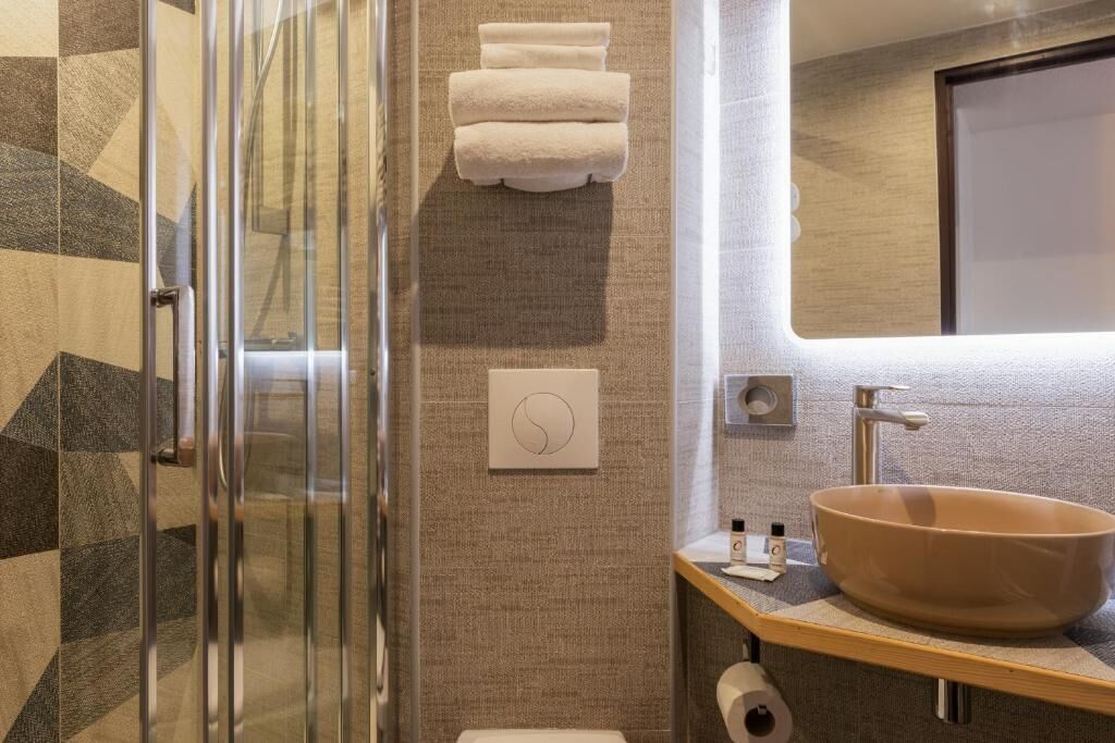 A modern bathroom with a glass shower enclosure, a wooden vanity with a large sink, and a towel rack with folded towels.