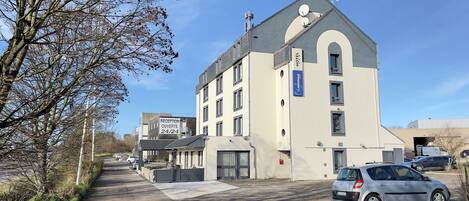 Un hotel con recepción abierta las 24 horas, un estacionamiento y un edificio de estilo arquitectónico moderno.