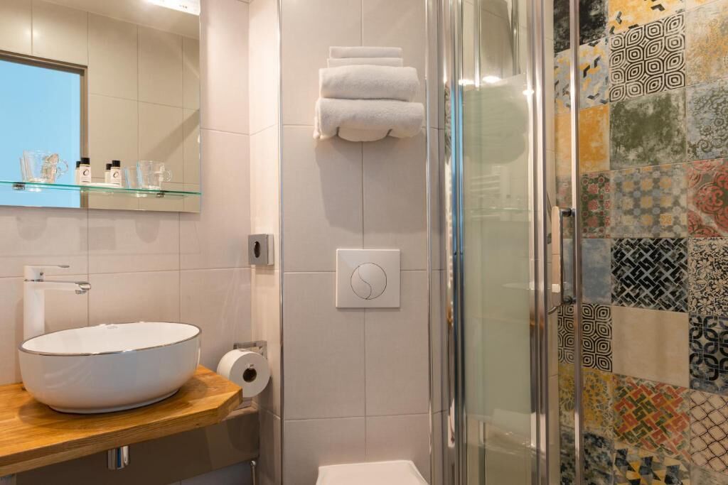 A bathroom with a large white sink, a glass shower enclosure, and a tiled wall with various patterns.