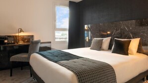 A hotel room with a large bed, a desk with a lamp, and a view of the sky through a window. - The Originals City, Hôtel Orléans Nord (Saran)