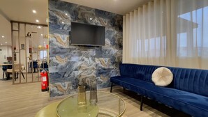A modern living room with a blue sofa, a glass coffee table, and a marble-patterned wall. - The Originals City, Hôtel Orléans Nord (Saran)