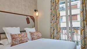 A hotel room with a large bed, a ceiling fan, a wall-mounted light, and a view of the outside balcony. - Hôtel Hiro (Paris)