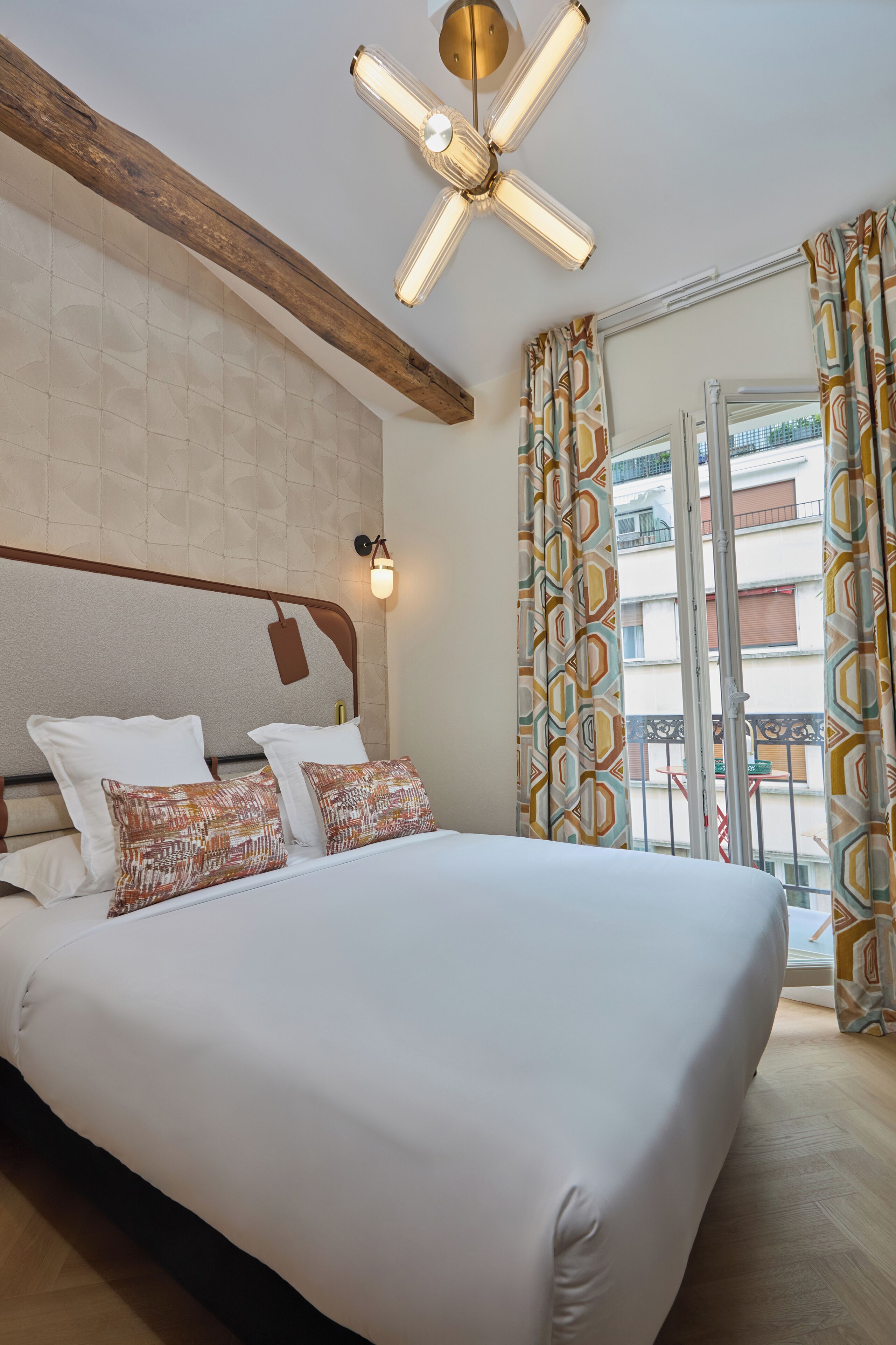 Habitación de hotel con una cama grande, ventilador de techo, luz fijada en la pared y vista al balcón exterior.