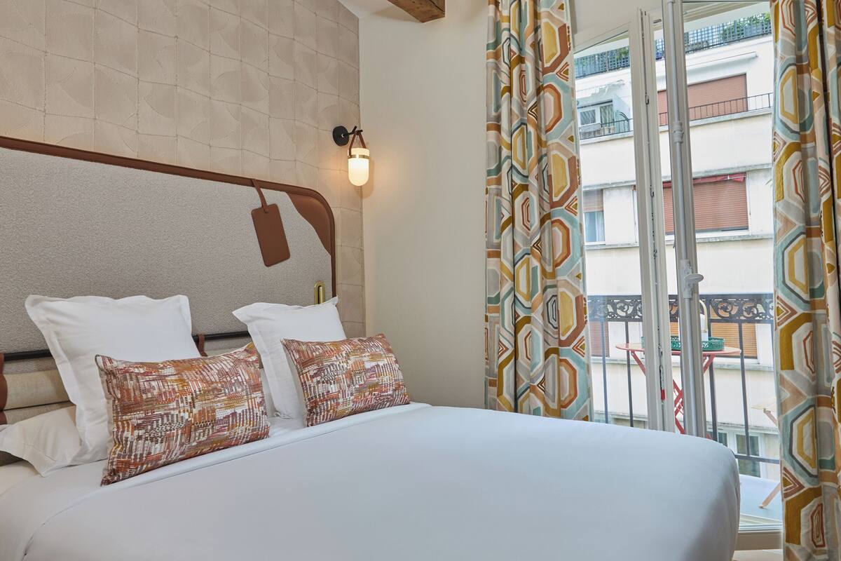 Quarto de hotel com uma cama grande, um ventilador de teto, uma luminária na parede e vista para a varanda externa.
