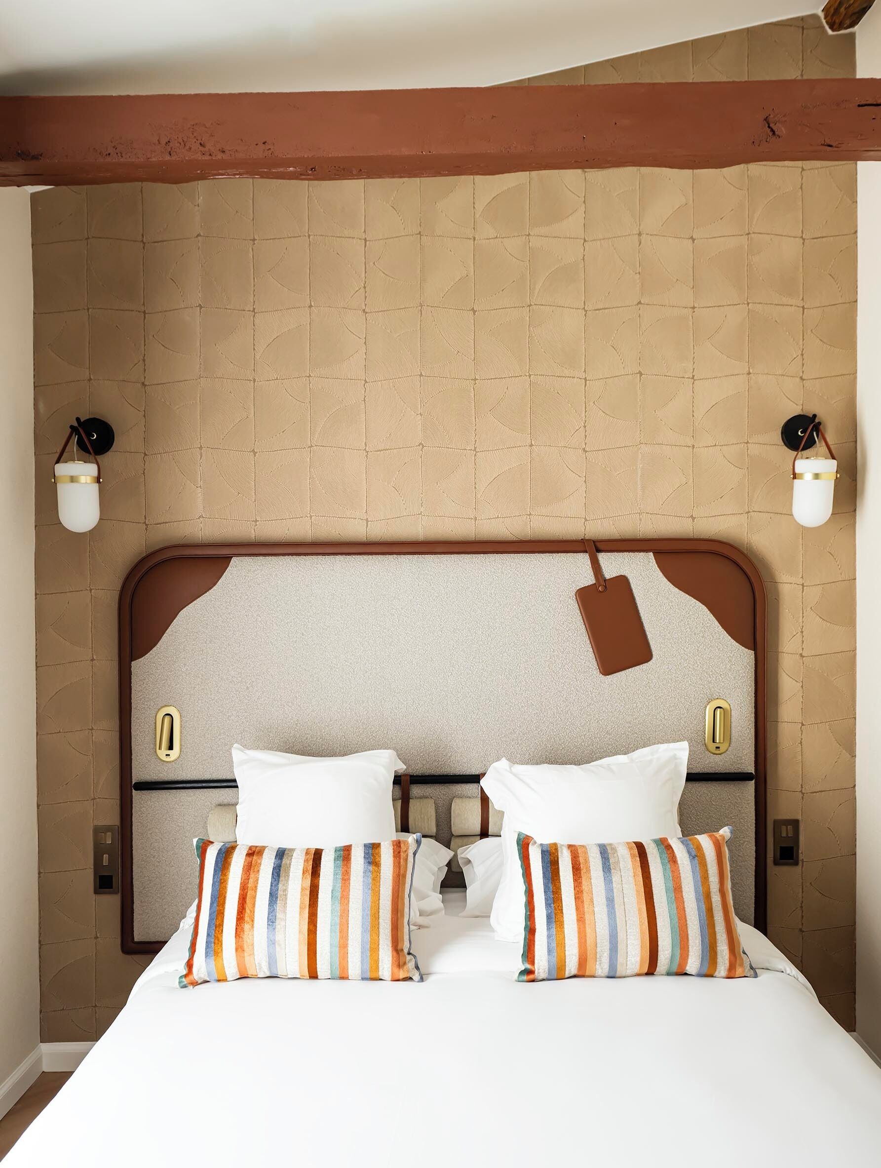Habitación de hotel con una cama grande, dos mesitas de noche, un cabecero con una etiqueta y dos lámparas fijadas a la pared.