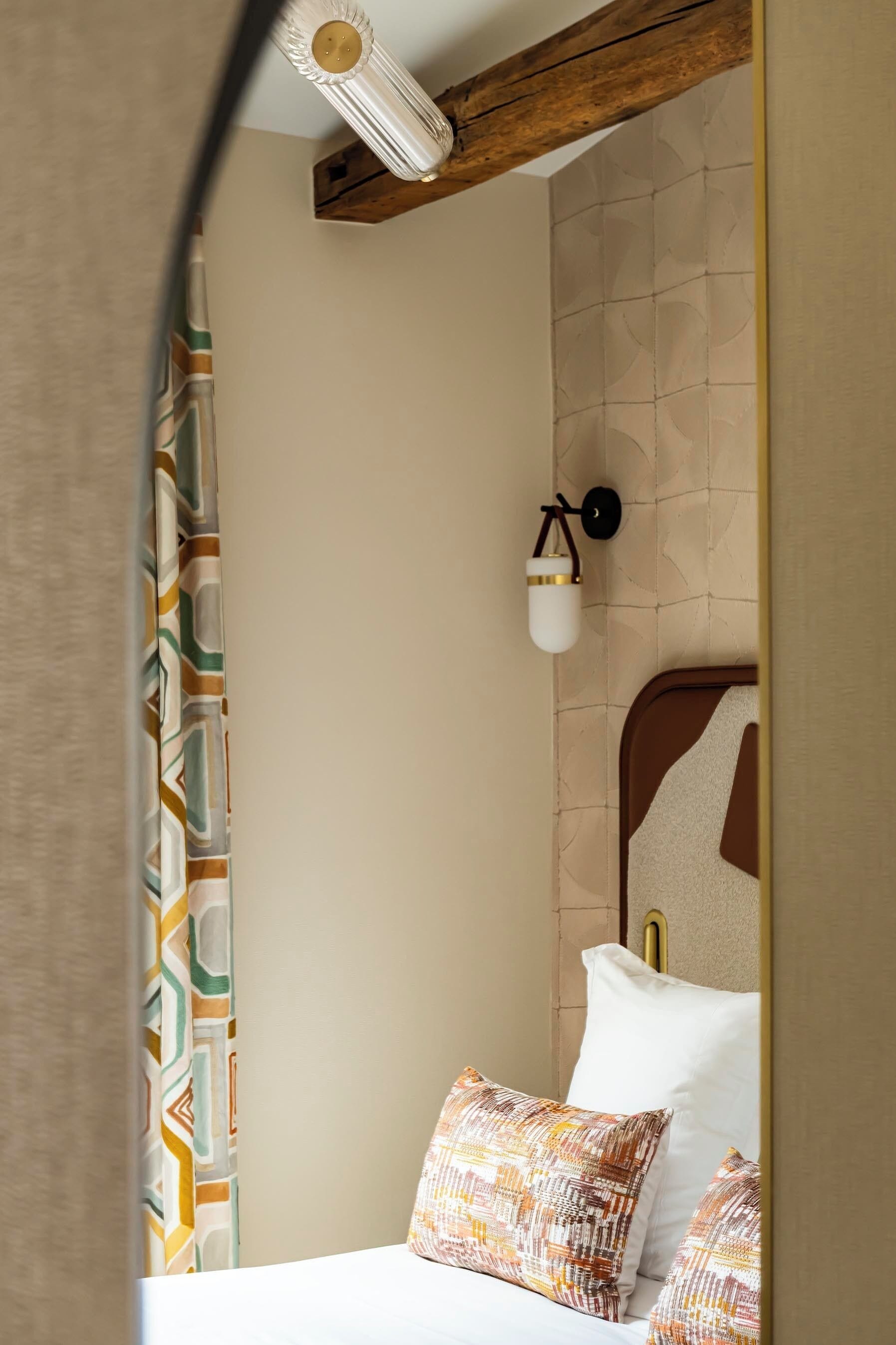 Quarto de hotel com cama, cortinas estampadas, luminária fixada na parede e parede texturizada.